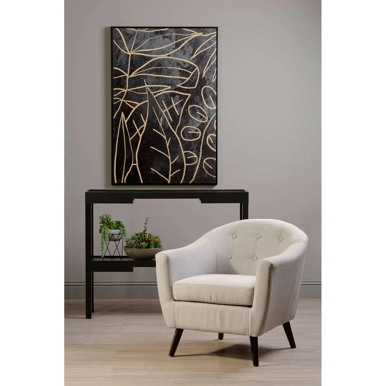 Light grey fabric armchair with button detailing beside black console table and wall art