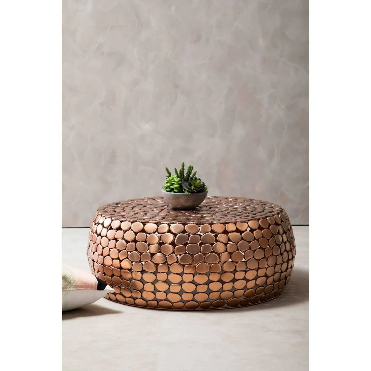 Round copper coffee table with textured surface and small plant decor