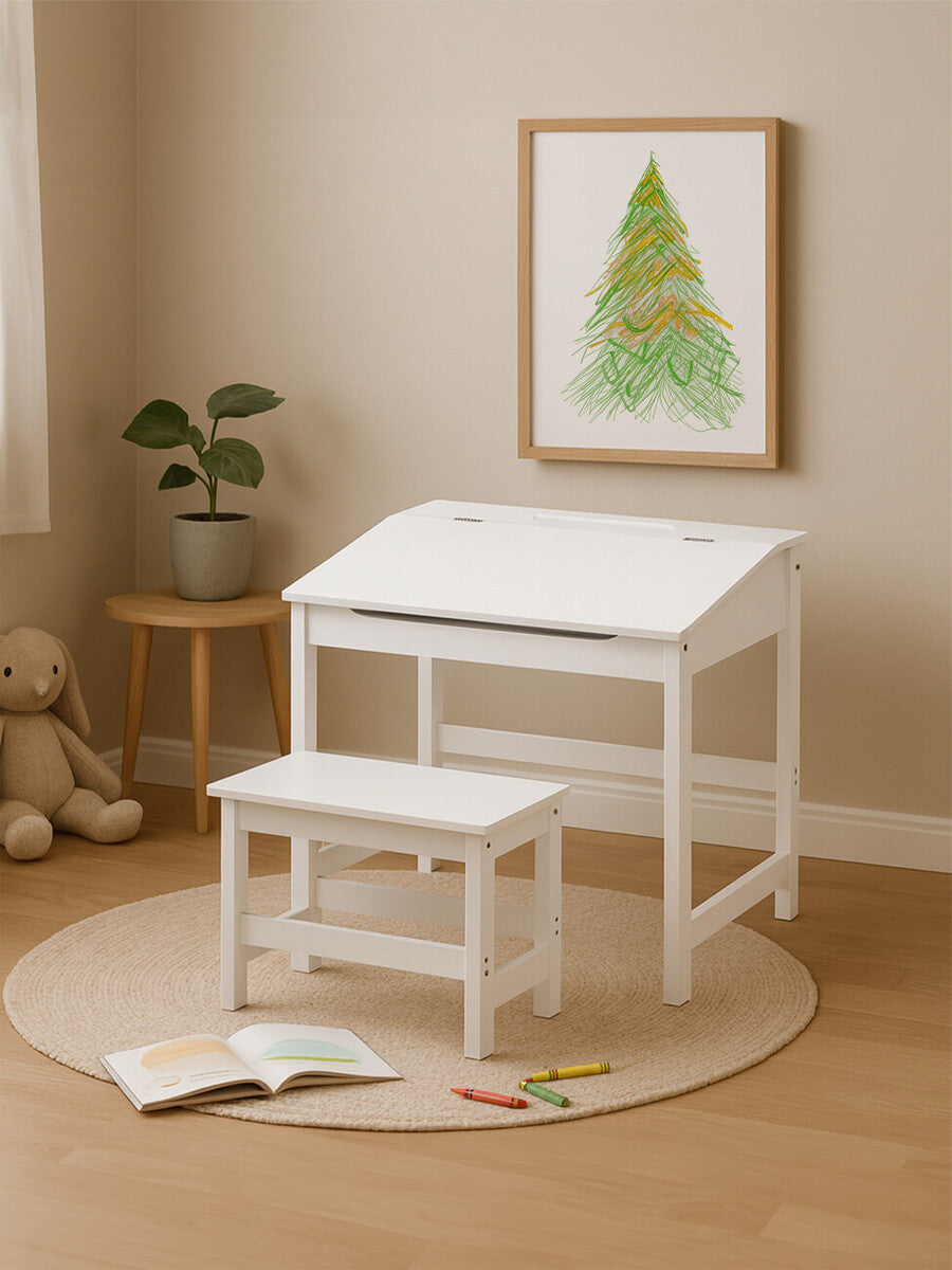 A white children's desk with a slanted top and a matching stool, placed on a round beige rug. A framed artwork featuring a green tree is hung on the wall above the desk, and a small potted plant is positioned next to the desk. Soft lighting enhances the warm, inviting atmosphere of the room
