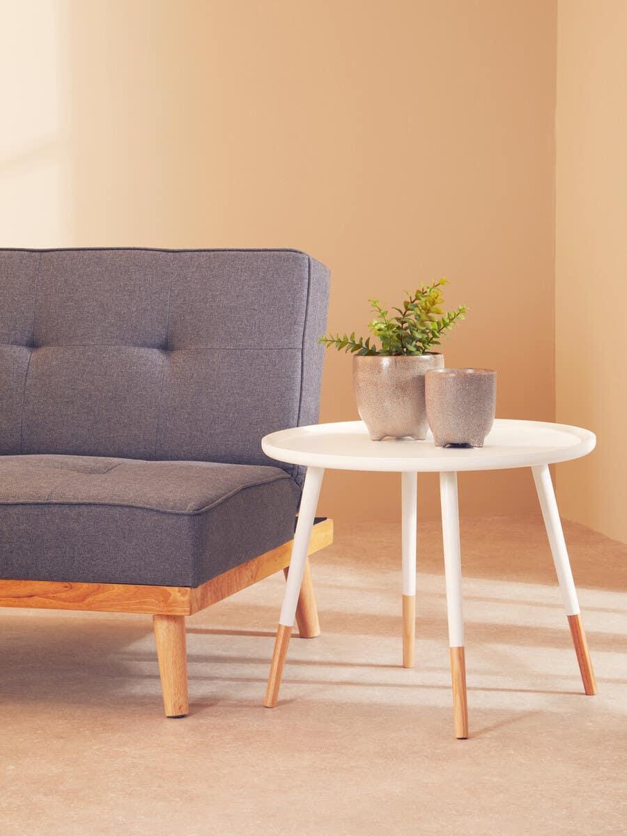 Grey fabric sofa with wood frame beside white round side table and ceramic plant pots