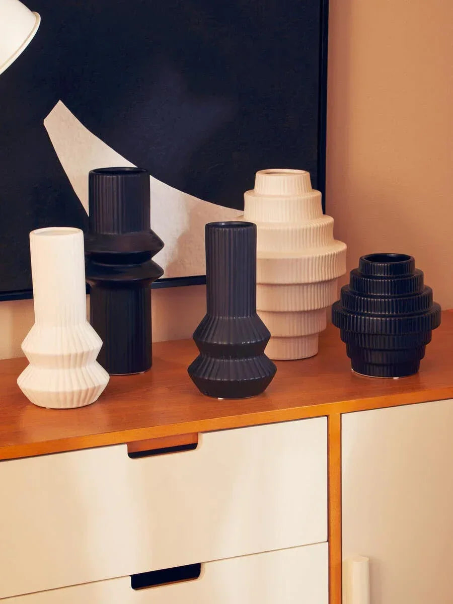 Modern ceramic vases in black and white with geometric shapes on wooden sideboard