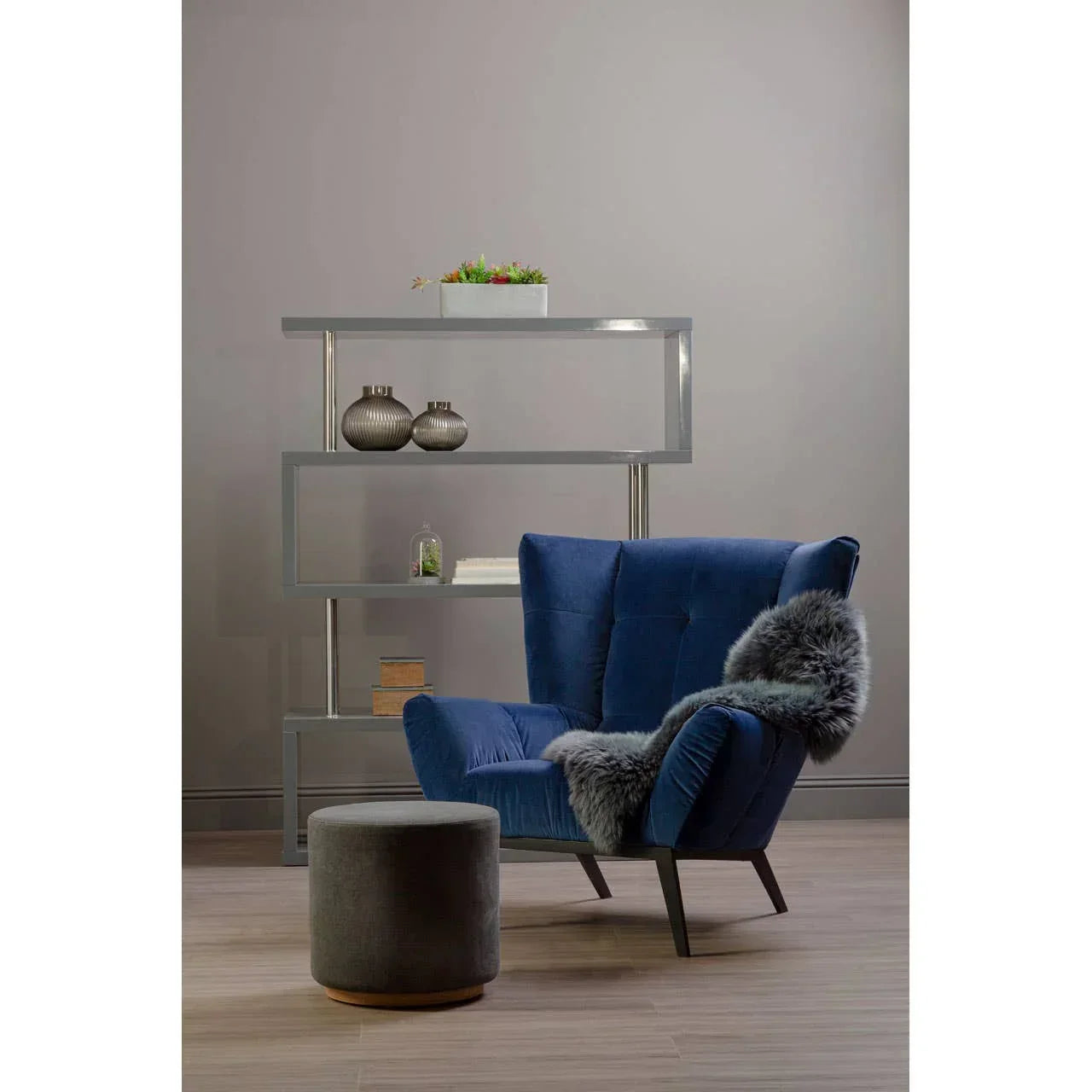 Blue accent chair with faux fur throw beside grey footstool and modern shelving unit