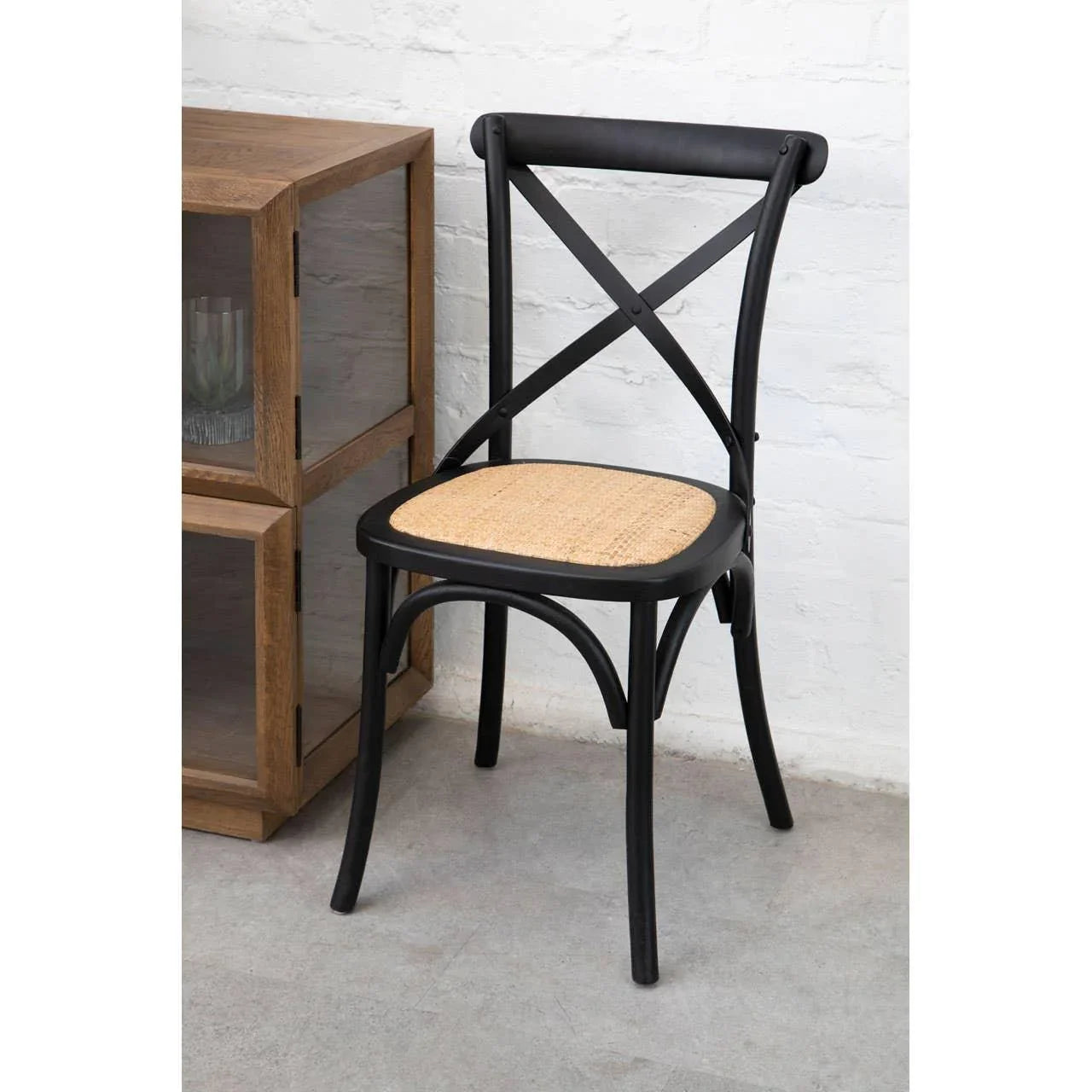 Black wooden dining chair with rattan seat and cross-back beside wooden cabinet
