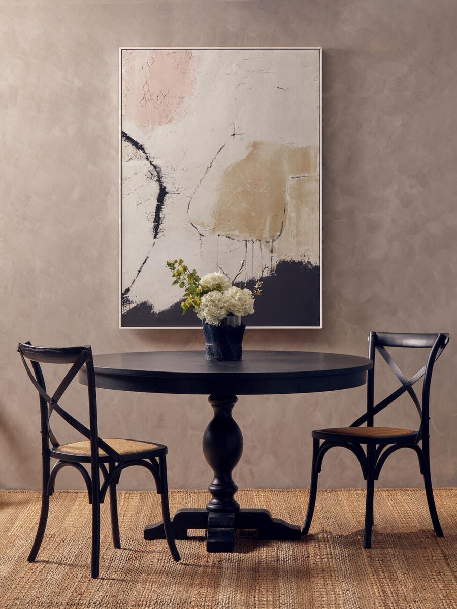 Black round dining table with pedestal base and two black chairs, floral centerpiece