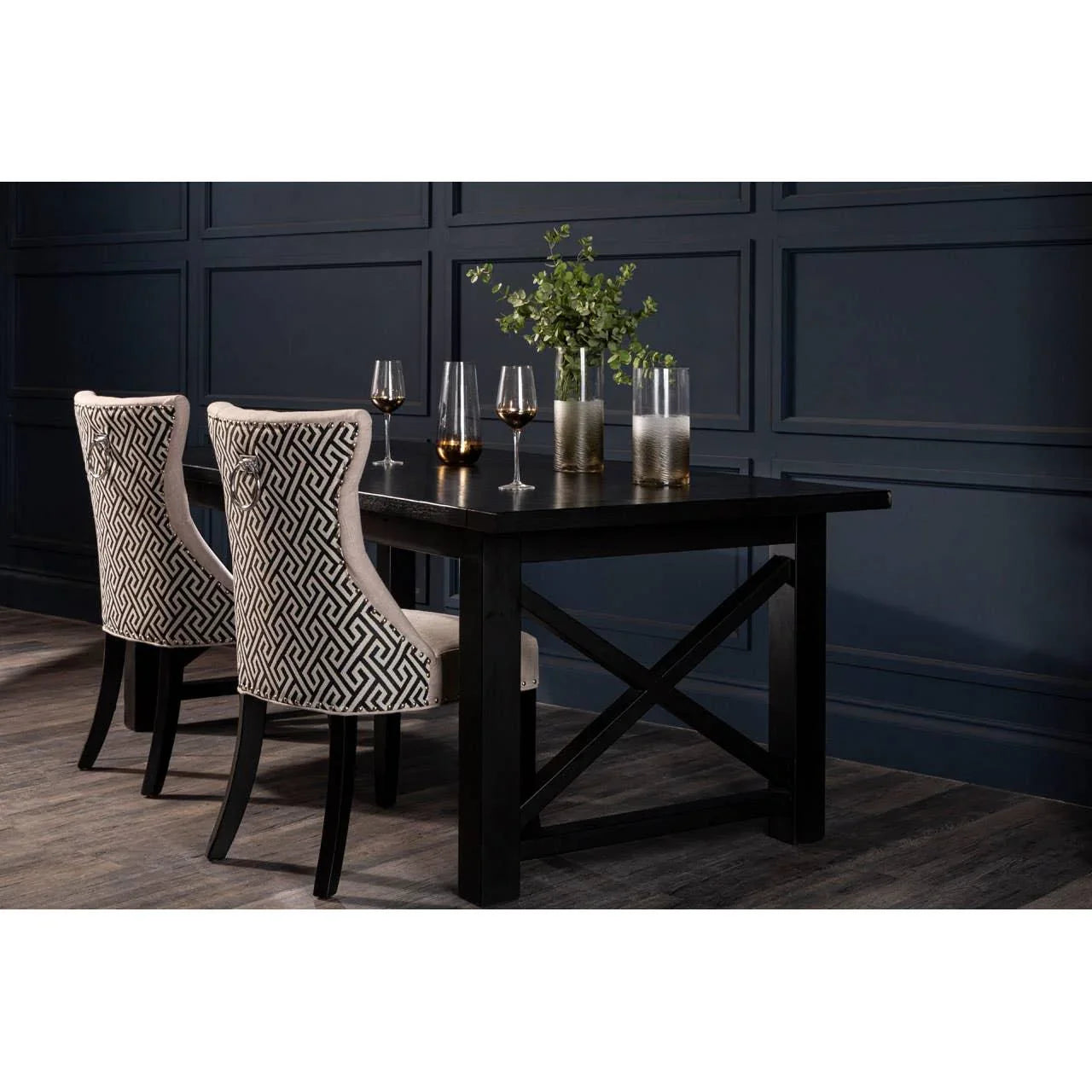 Rectangular black dining table with two patterned upholstered chairs and glassware