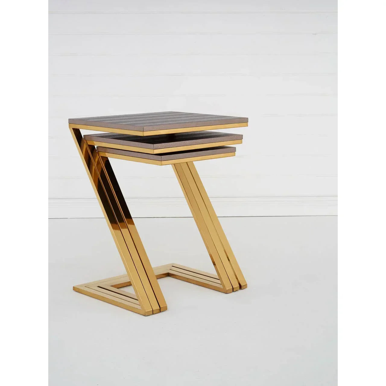 Set of gold metal nesting tables with dark wood tops against white wall