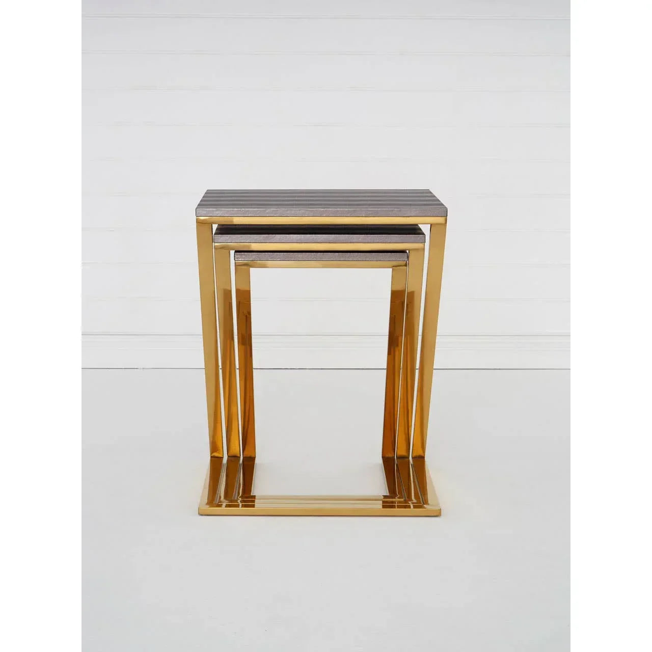 Gold metal nesting tables with dark tabletops set against a white wall