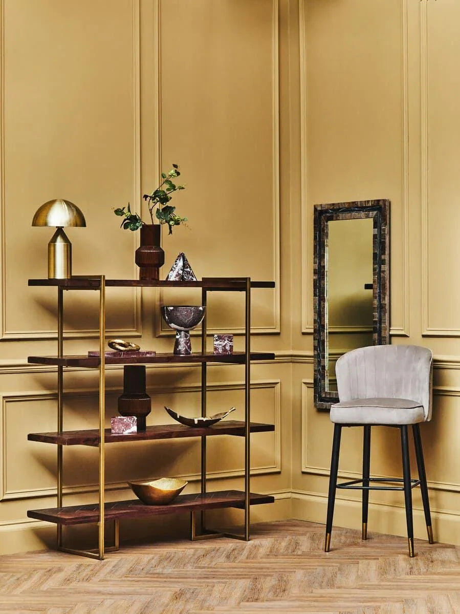 Gold and wood shelving unit with decor beside grey velvet bar stool in modern living room