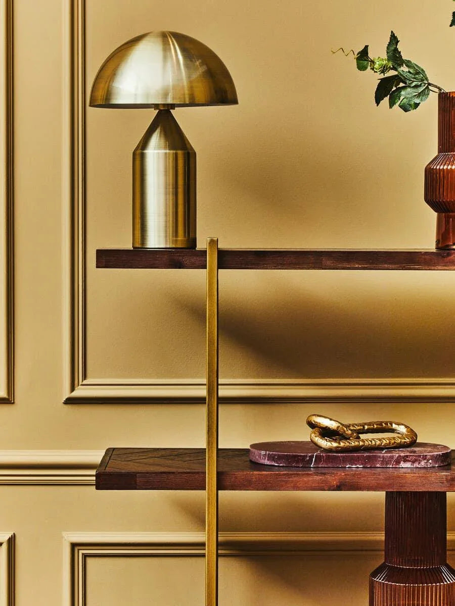 Brass table lamp on wooden shelf with decorative vase and gold accent sculpture