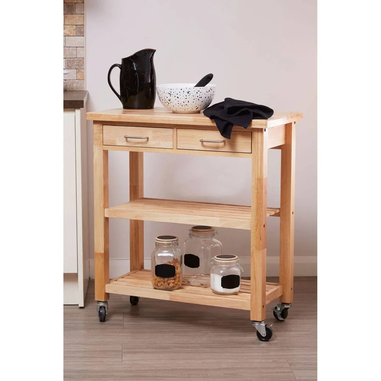 Wood kitchen trolley with two drawers, shelves, and casters, holding jars and kitchenware