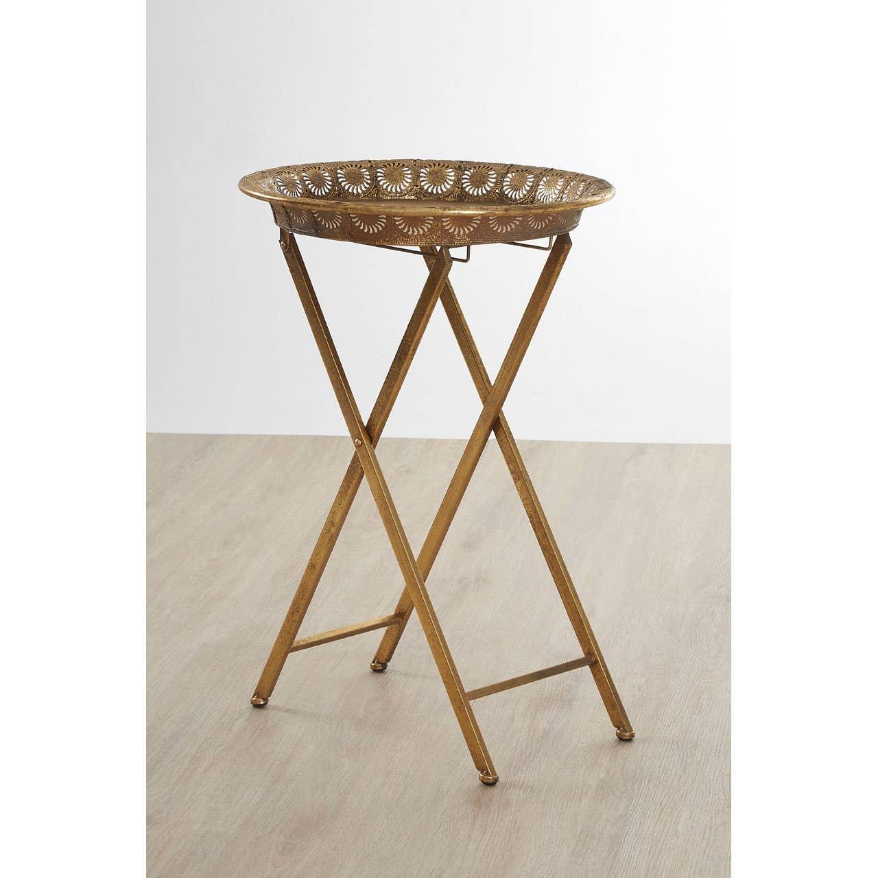 Gold metal folding side table with decorative cutout tray top on light wood floor