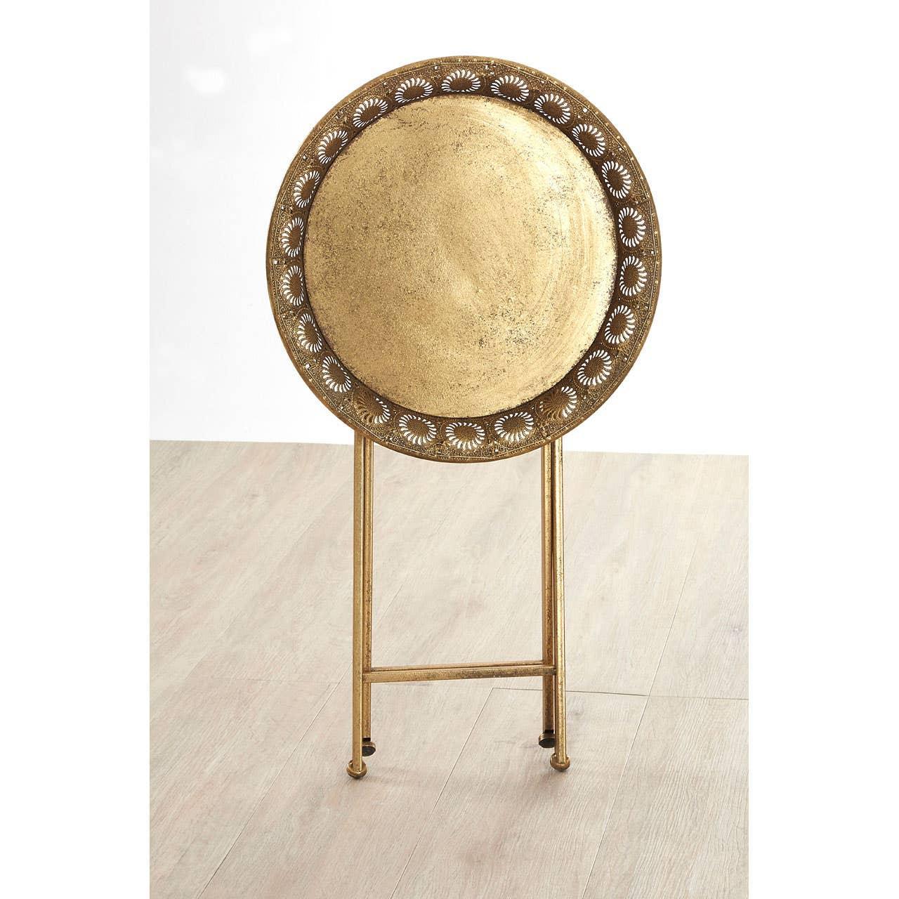 Round gold metal tray table with decorative cut-out pattern, standing on folding legs