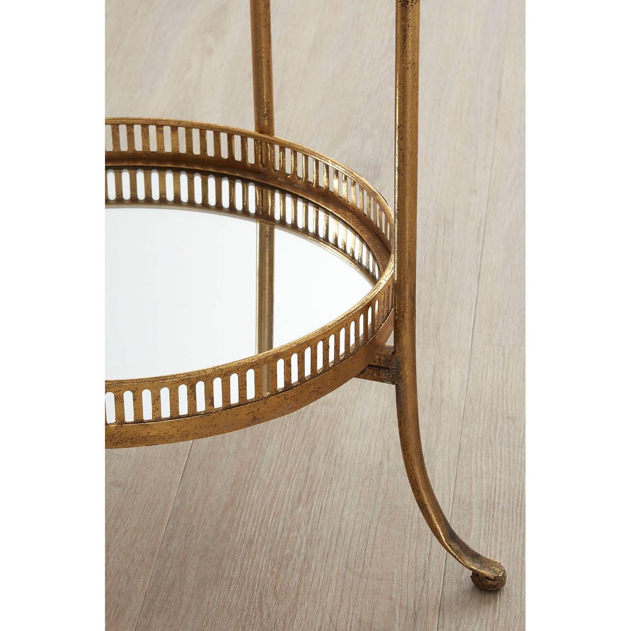 Gold metal side table with mirrored lower shelf and decorative openwork edge on wood floor