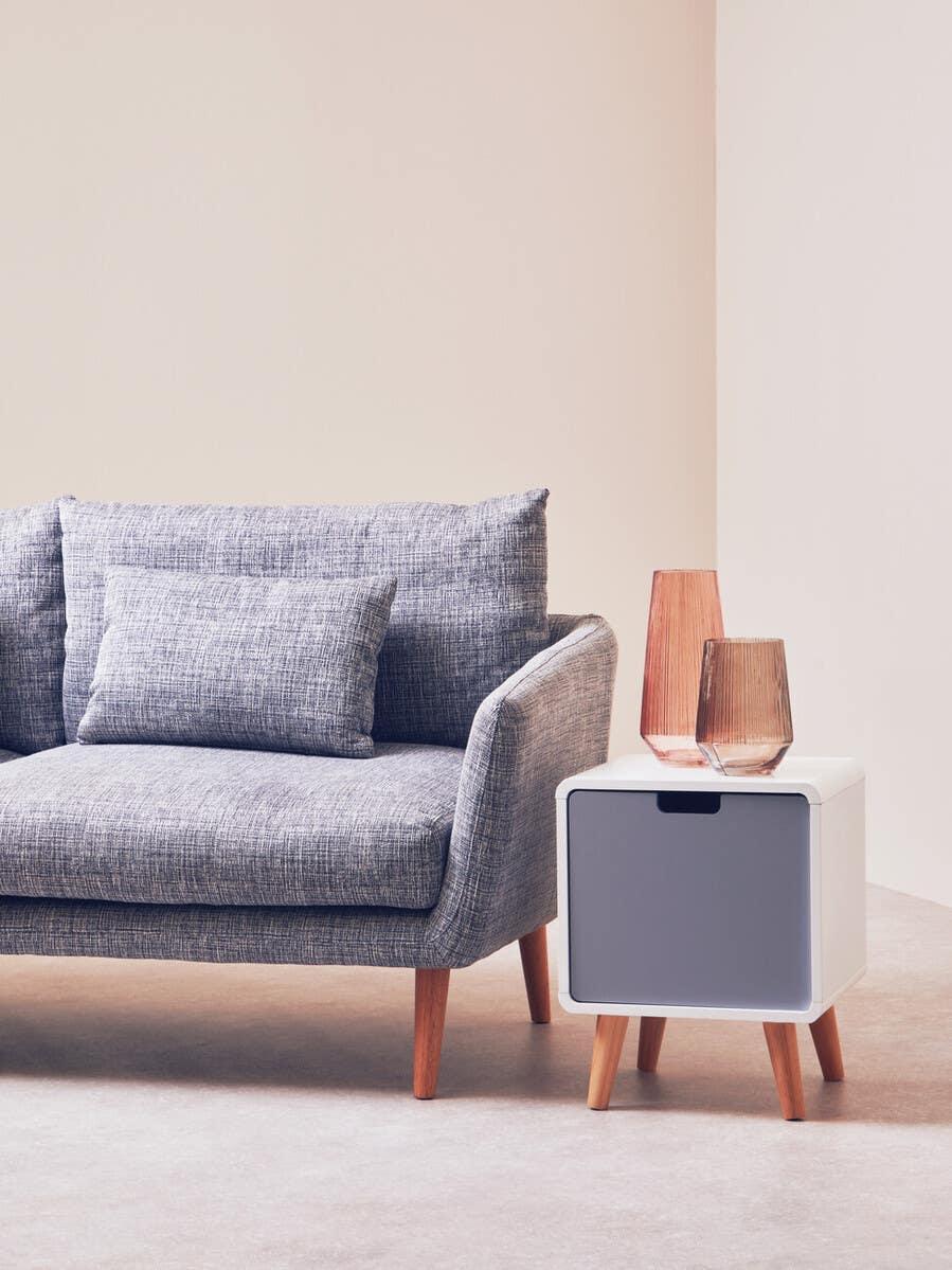 Grey fabric sofa with wooden legs beside modern white and grey side table with glass vases