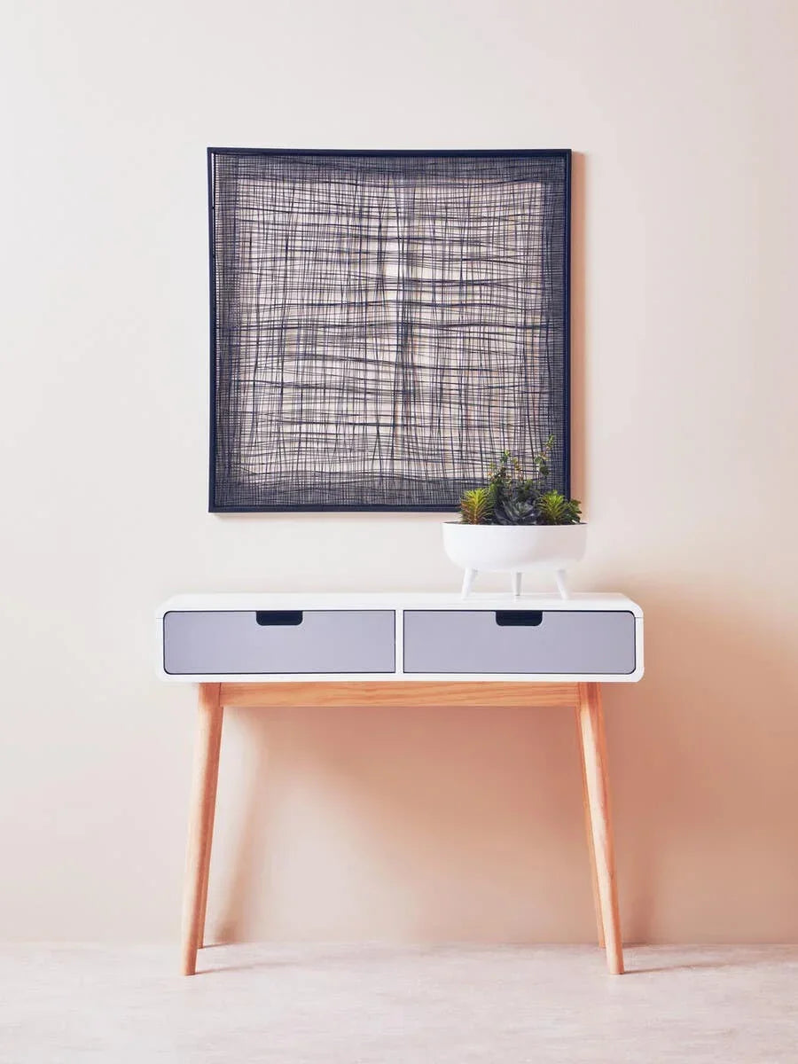 Modern console table with light wood legs, dual grey drawers and white planter, wall art above