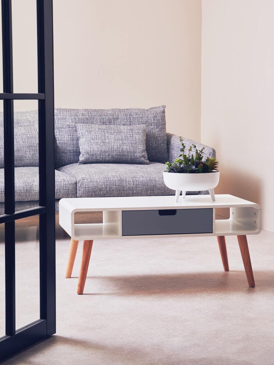 Grey fabric sofa with cushions behind white modern coffee table and potted plant