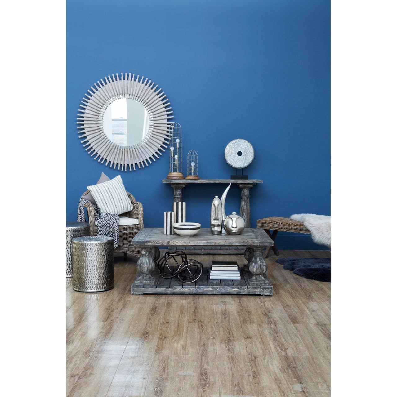 Rustic wooden coffee table and rattan armchair in blue accent living room with round mirror