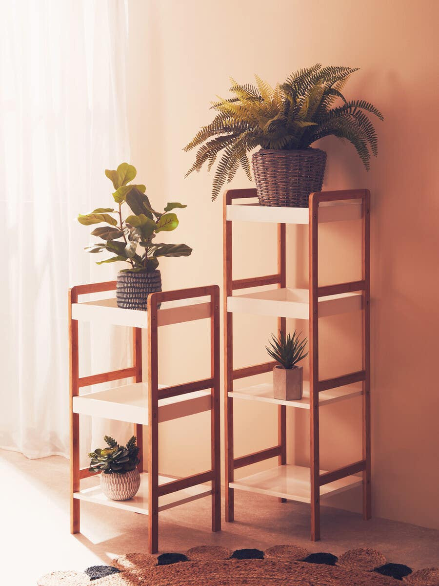 Four-tiered shelf unit featuring a combination of white and natural wood finishes, with two potted plants on the top shelves. The unit has an open design, showcasing its spacious tiers and minimalist style, set against a softly lit background