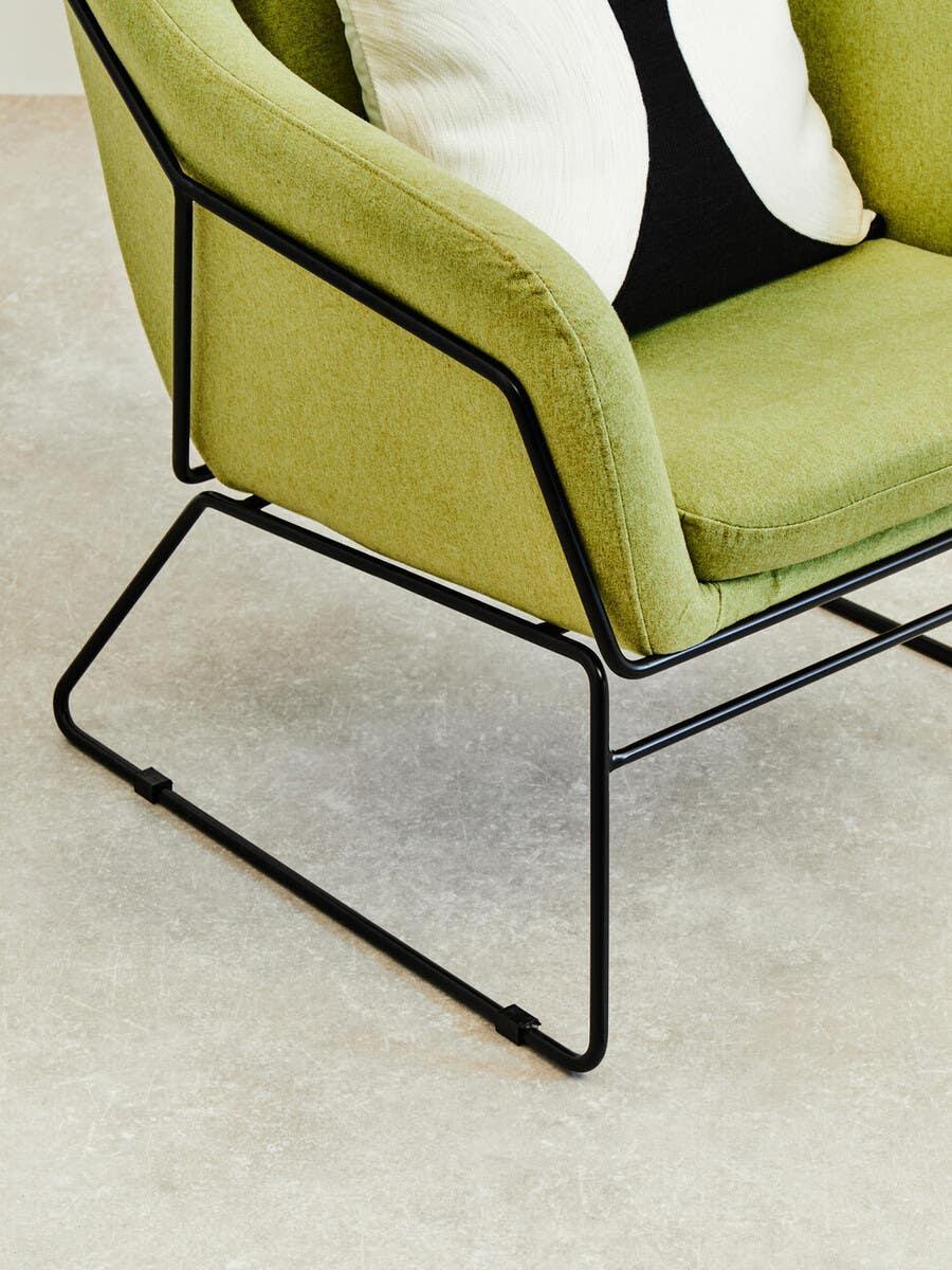 Green upholstered armchair with black metal legs and modern cushion on light floor