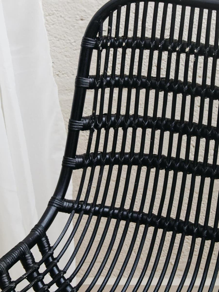 Curved black rattan chair with a sleek, modern design featuring horizontal and vertical woven patterns, showcasing a natural texture and a minimalist aesthetic. The chair's backrest is gently arched, providing a comfortable seating option