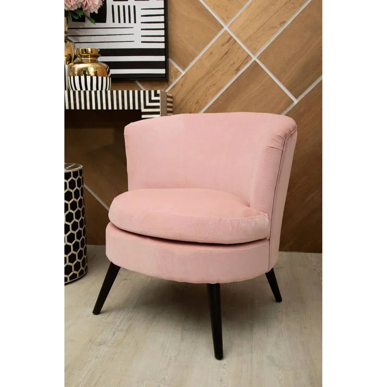 Blush pink accent chair with curved backrest and black wooden legs in modern room setting