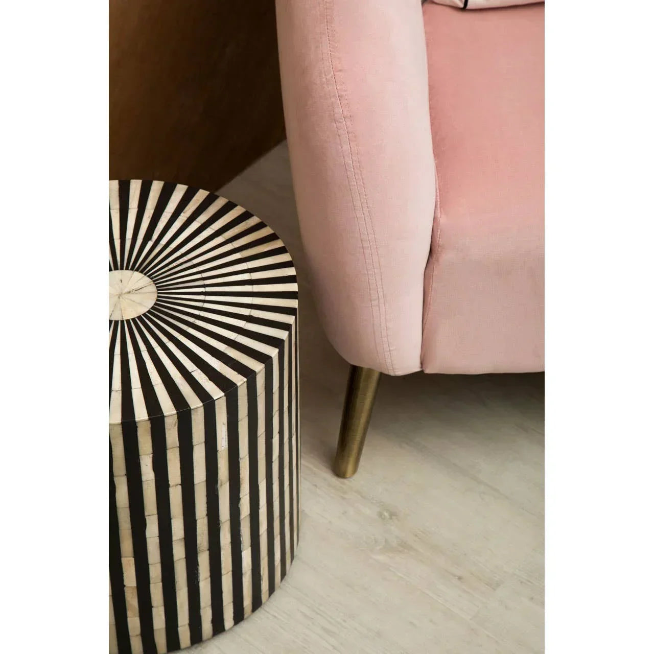 Black and white striped side table next to pink velvet armchair with gold leg