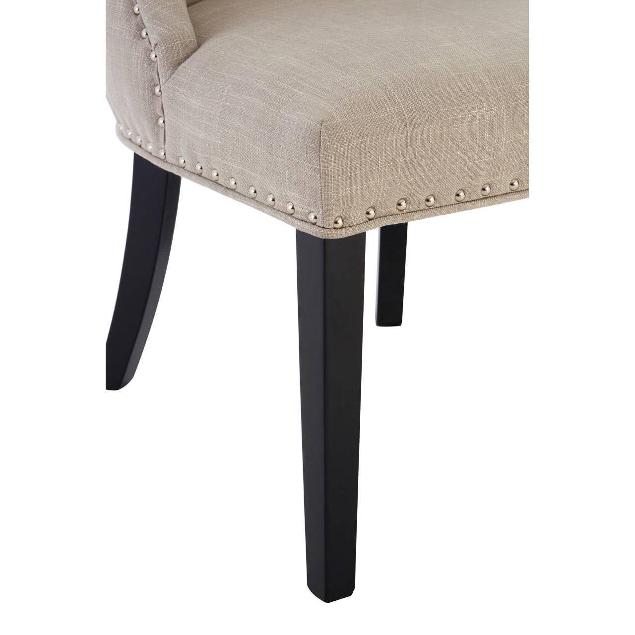 Beige upholstered dining chair with black wooden legs and silver stud detailing, close view