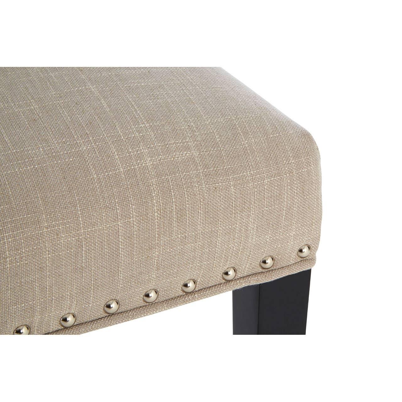 Beige fabric dining chair seat with silver nailhead trim and dark wooden leg close-up