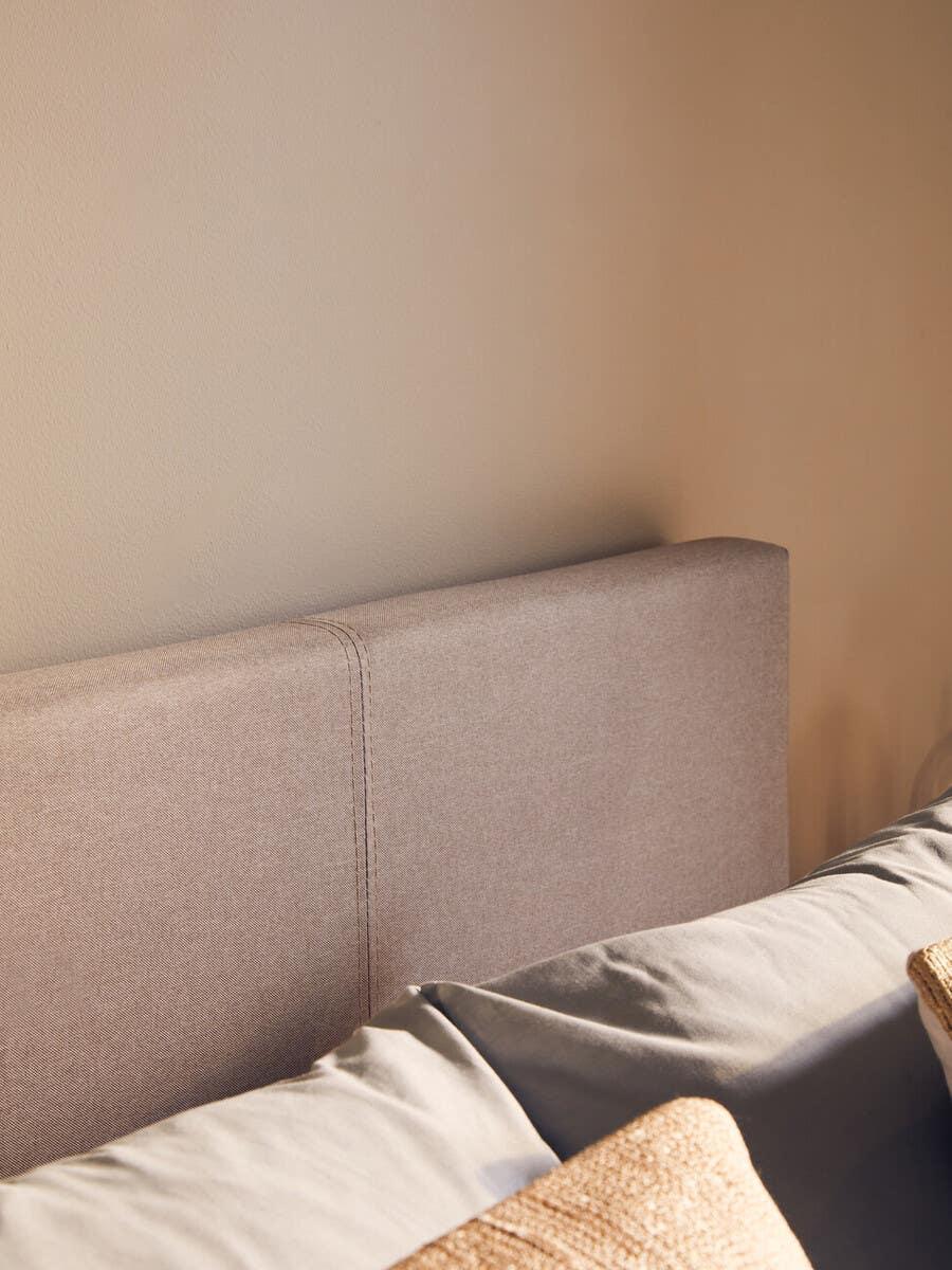 Beige fabric bed headboard with stitched detail and neutral bedding in bright bedroom