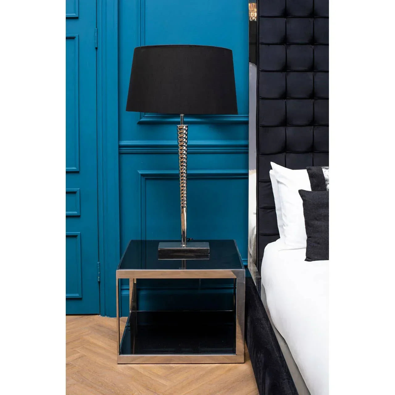 Chrome and black table lamp on modern glass bedside table beside upholstered bed