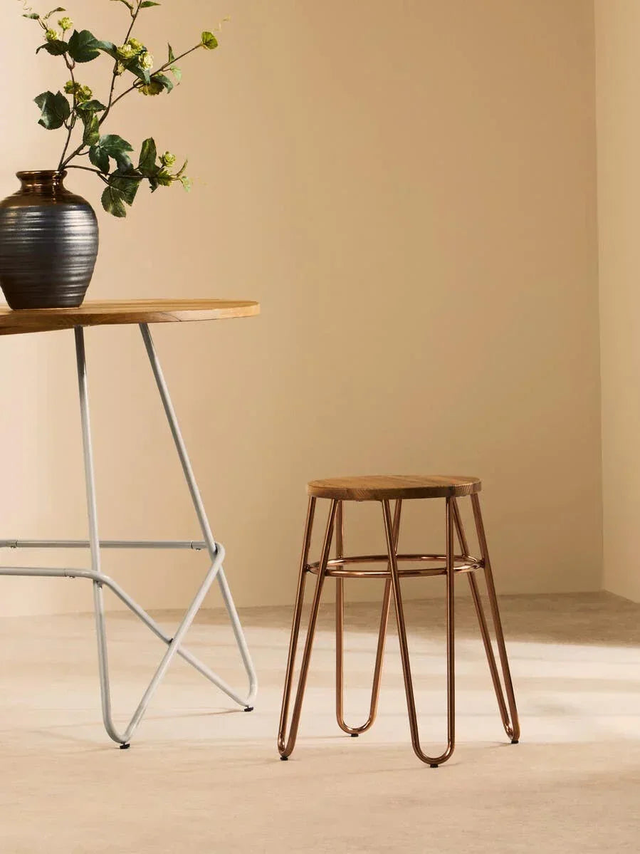 Wooden seat bar stool with copper metal legs beside table in minimalist room