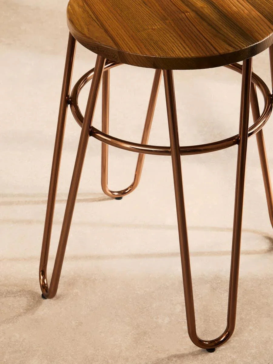 Round wooden bar stool with copper metal legs on stone floor