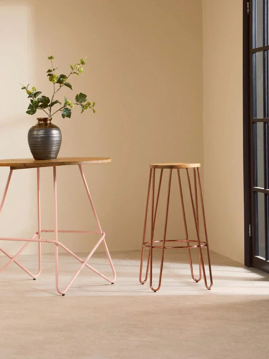 Metal bar stool with copper finish beside wood and metal table in bright room