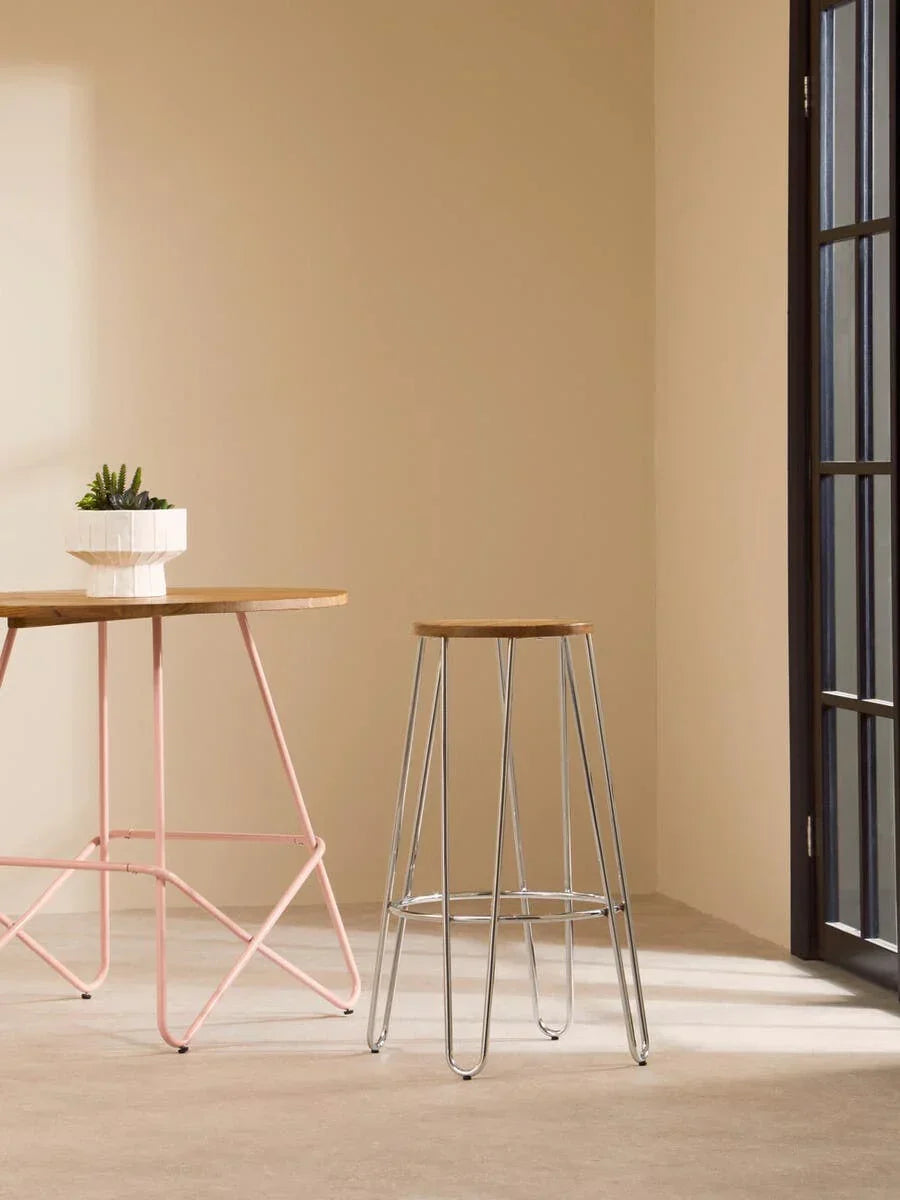 Metal bar stool with wooden seat beside light pink table in sunlit modern room
