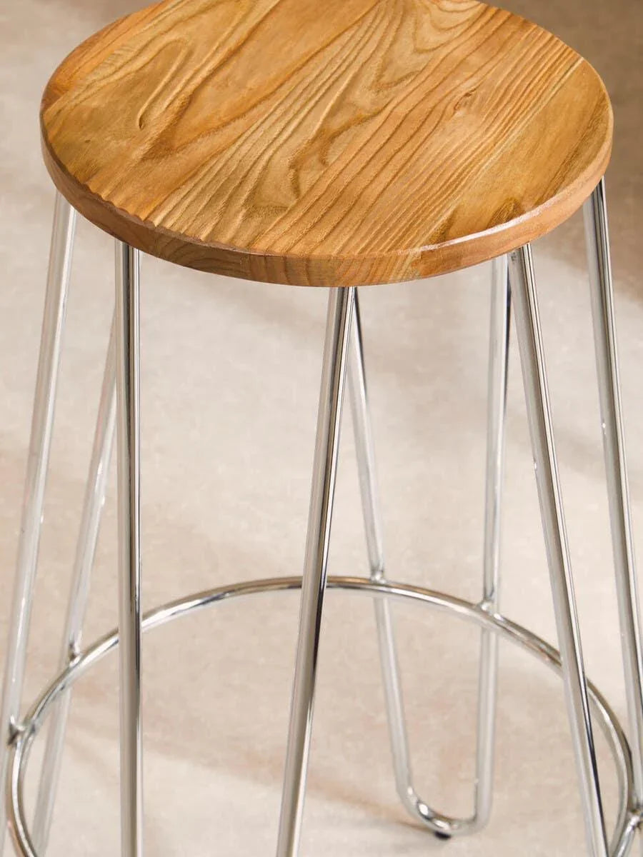 Bar stool with round wooden seat and chrome metal legs on light tile floor