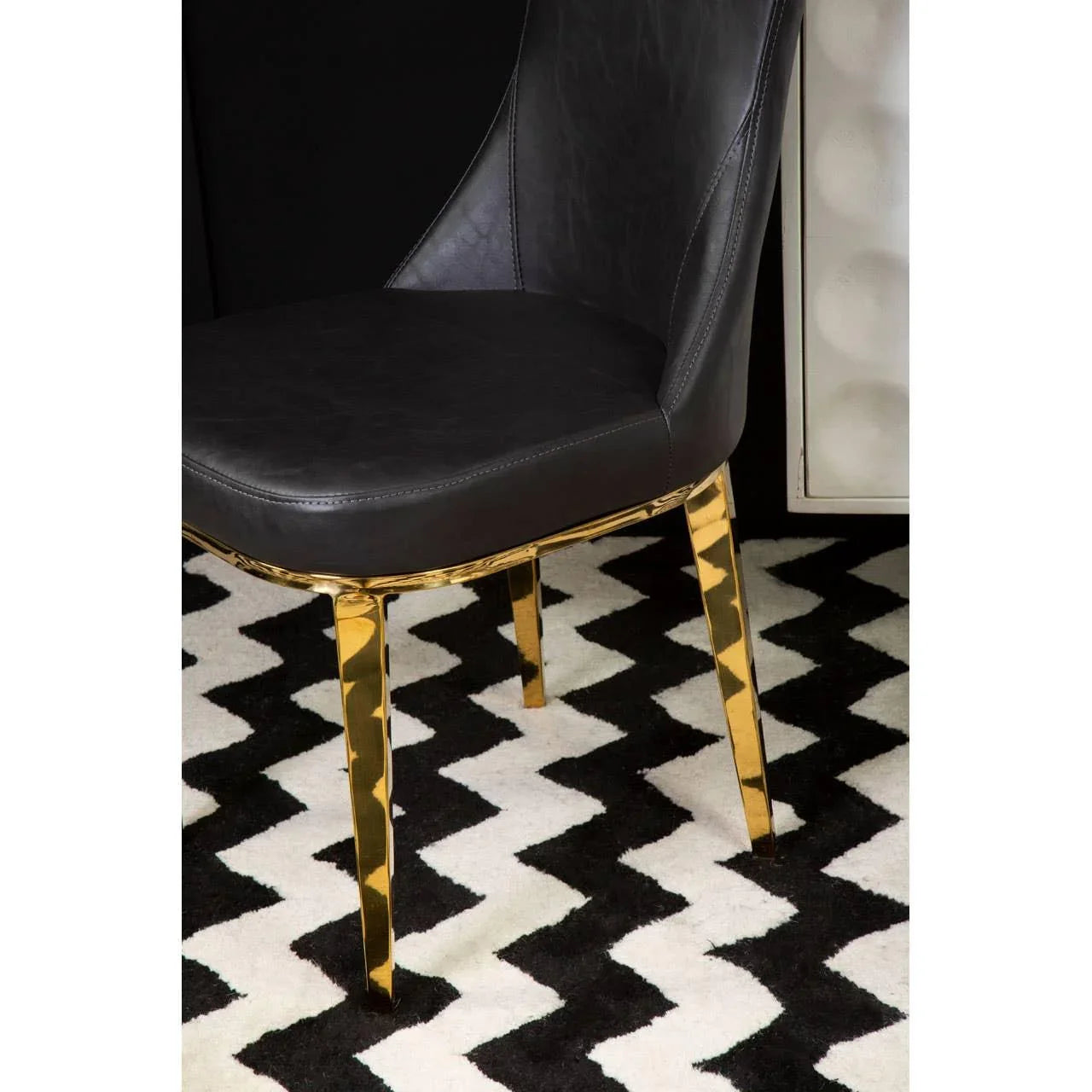 Black leather dining chair with gold legs on black and white zigzag rug