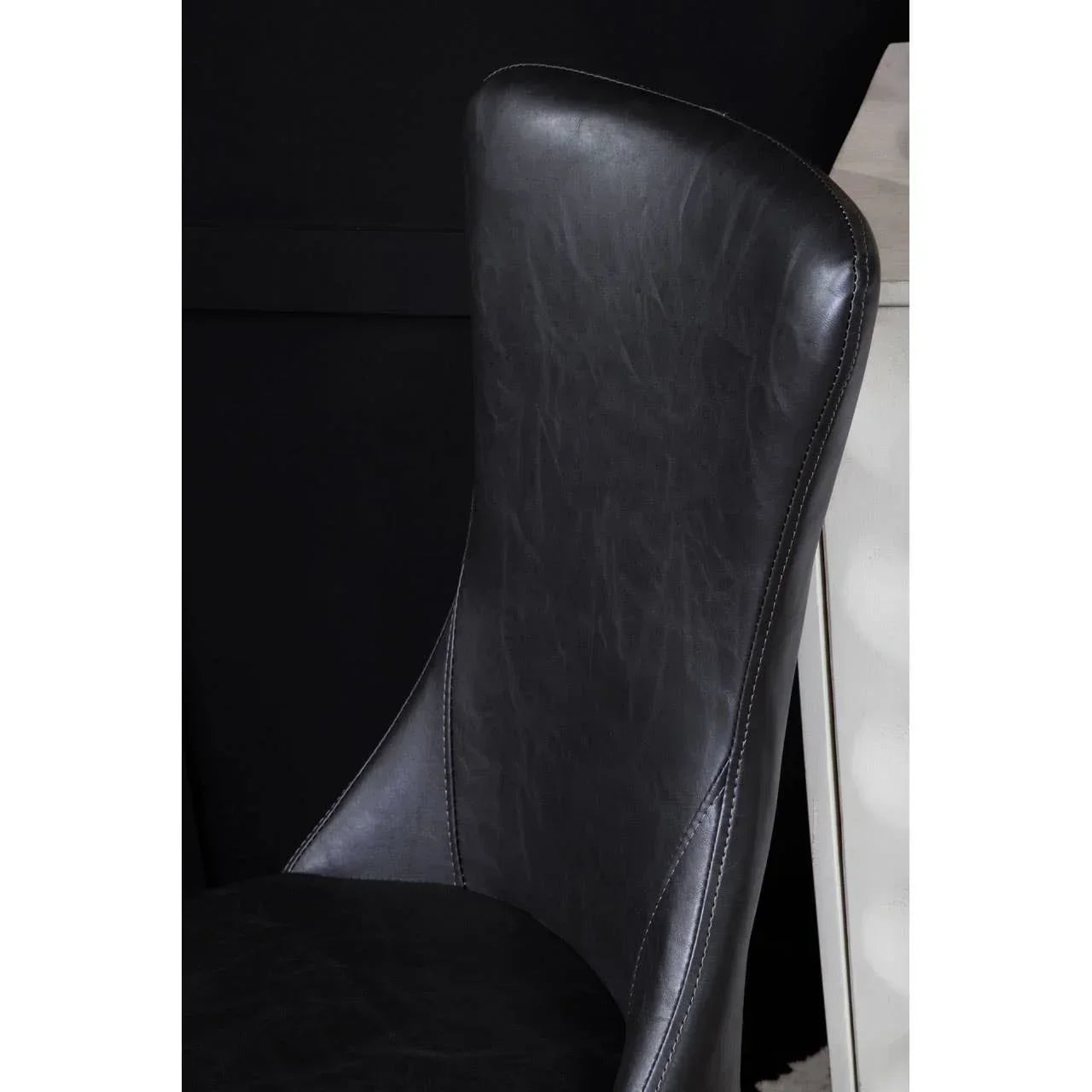 Black faux leather dining chair with curved backrest and detailed stitching