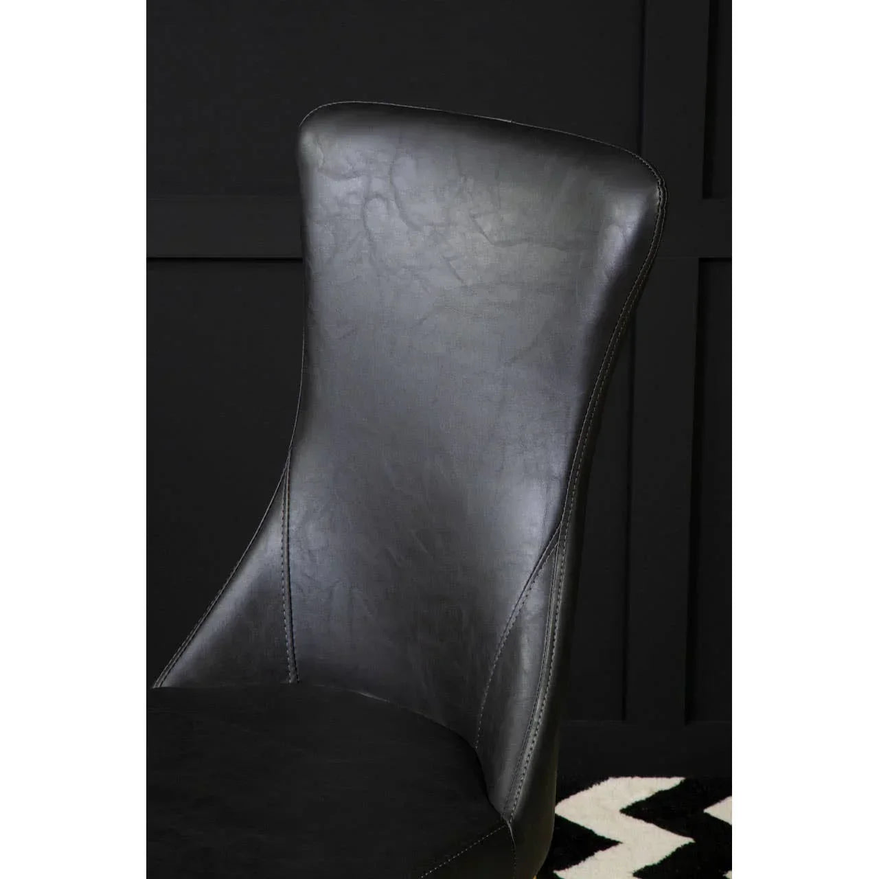 Black faux leather dining chair with curved backrest against dark wall