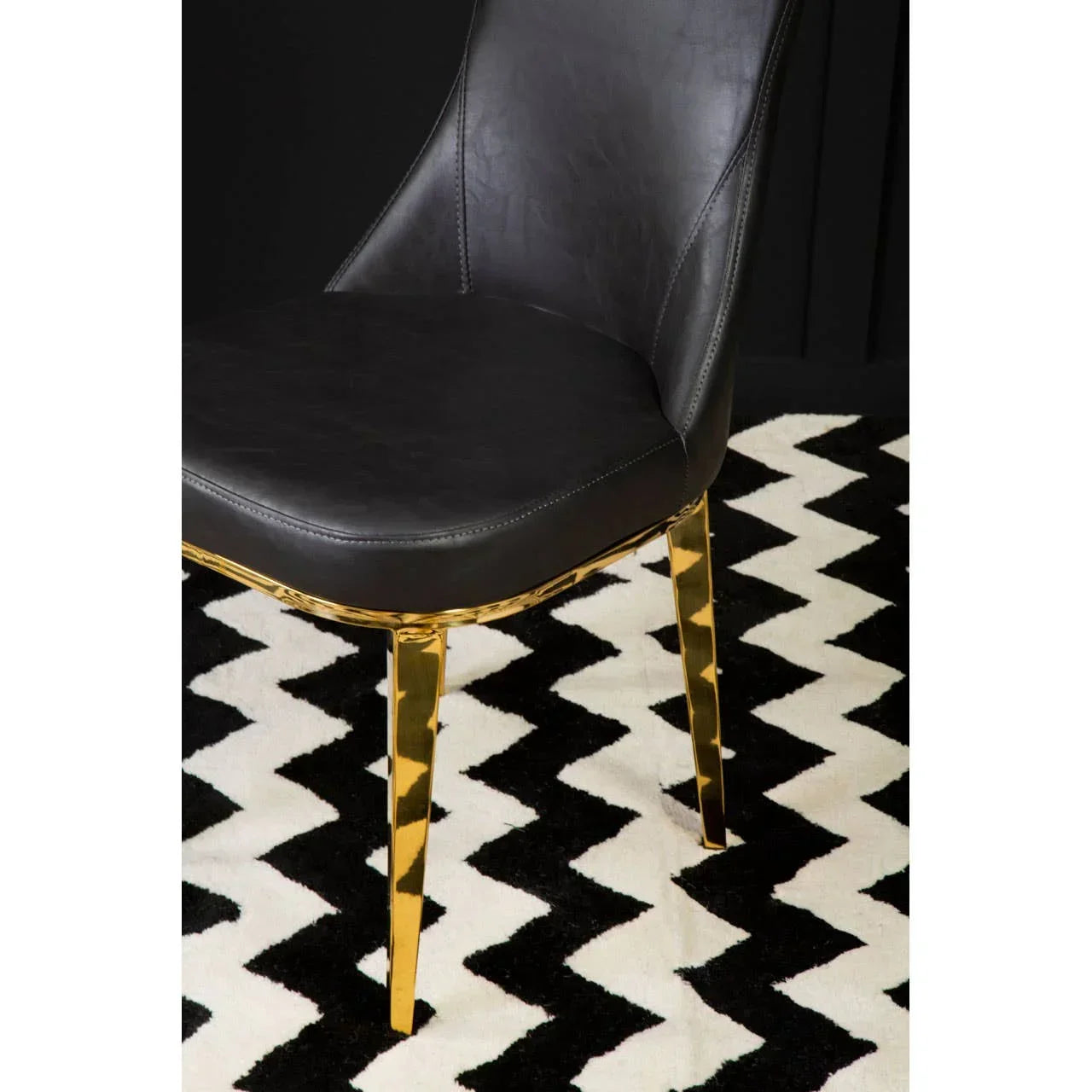 Black leather dining chair with gold legs on zigzag patterned rug