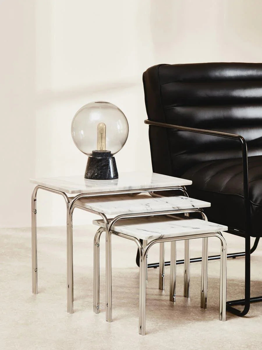 nest of marble effect side tables with chrome legs beside black leather armchair