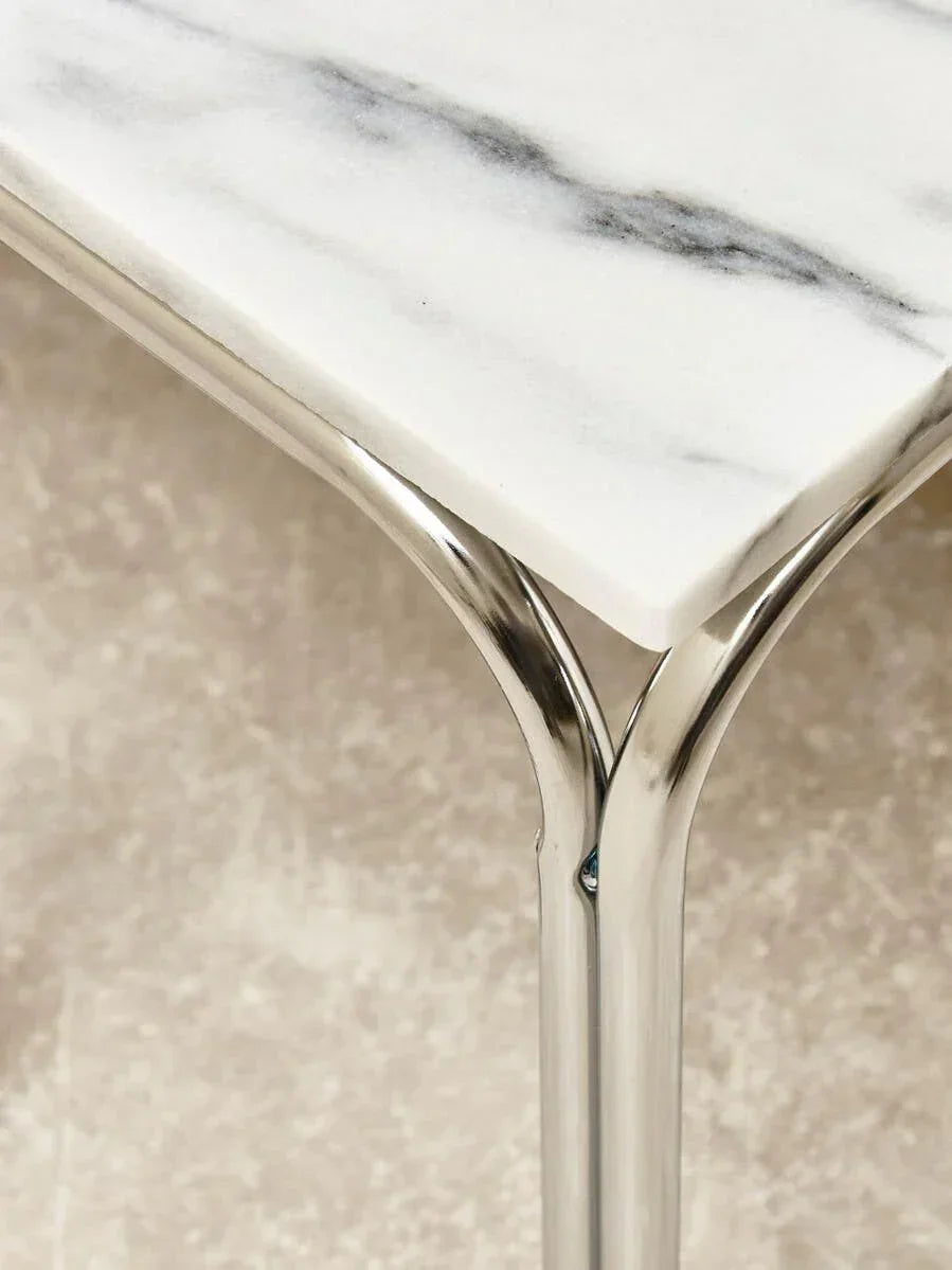 Corner of marble dining table with chrome metal leg on neutral textured floor