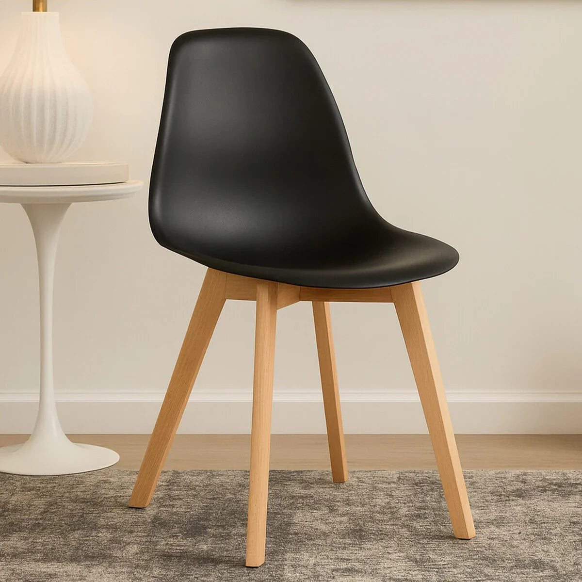 Black dining chair with curved seat and wooden legs on grey rug near round side table