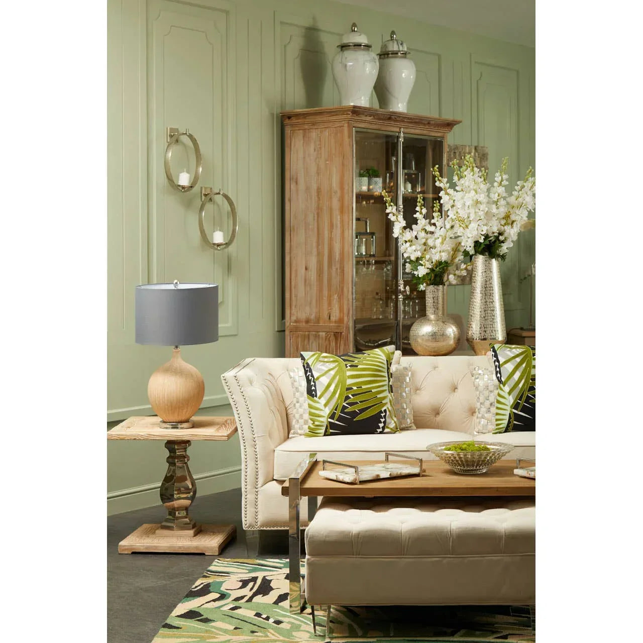 Beige fabric sofa with green leaf cushions, wooden coffee table, and display cabinet in living room