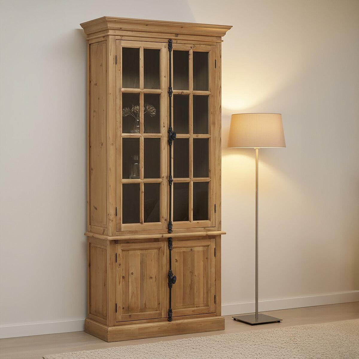 Tall cabinet made of pine wood featuring four doors with glass panels on the upper section and solid wood panels on the lower section. The cabinet has a natural wood finish, showcasing its grain, and is positioned against a light-colored wall next to a modern floor lamp