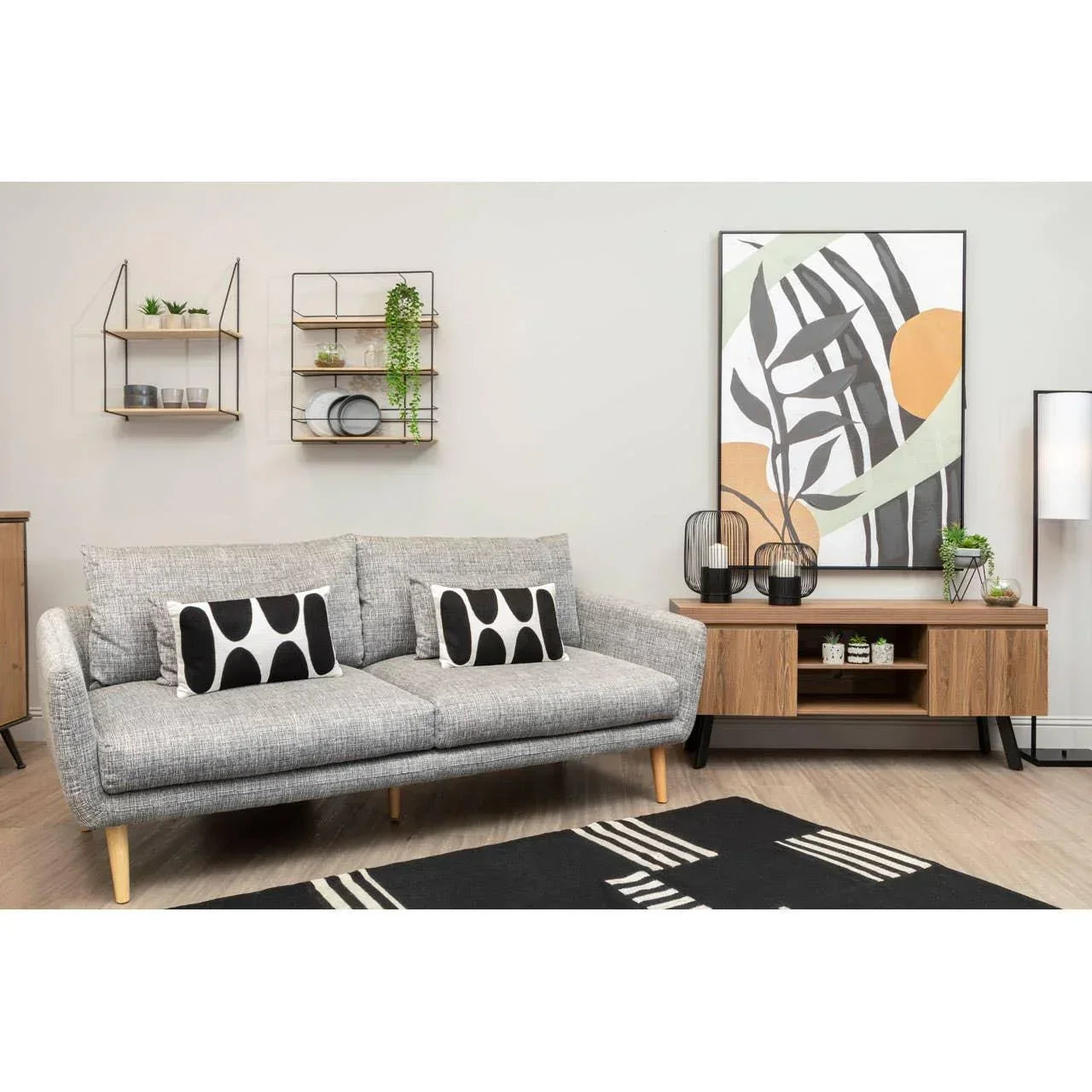 Grey fabric sofa with black and white cushions in modern living room with sideboard and wall art