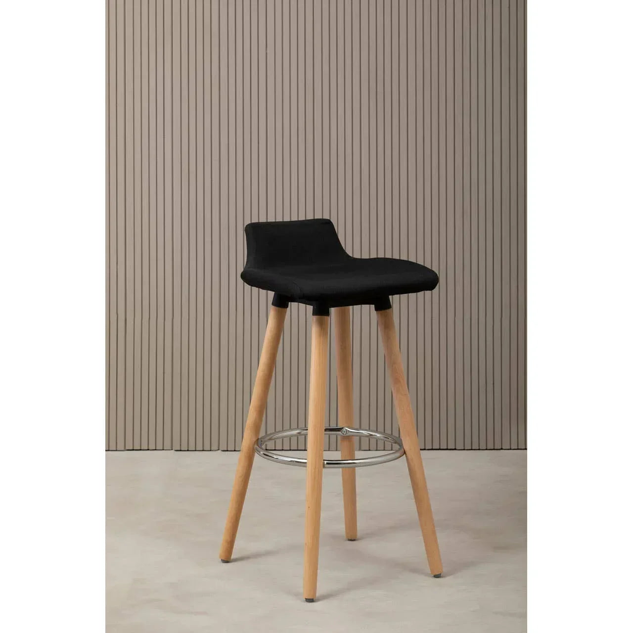 Black bar stool with wooden legs and metal footrest against neutral wall
