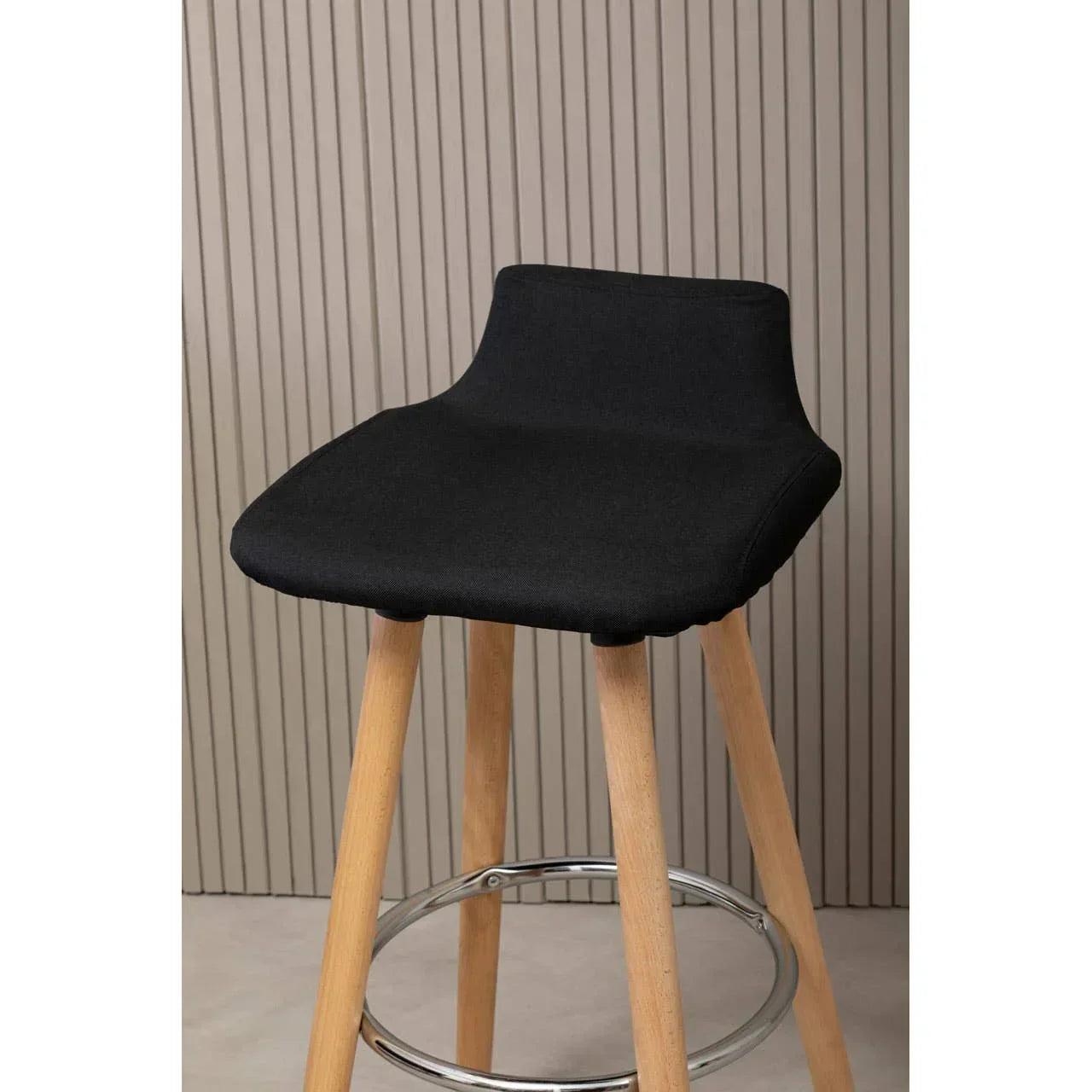Black fabric bar stool with wooden legs and chrome footrest against panelled wall