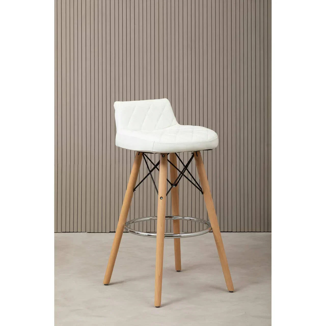 White bar stool with wooden legs, metal footrest, and quilted backrest against panel wall