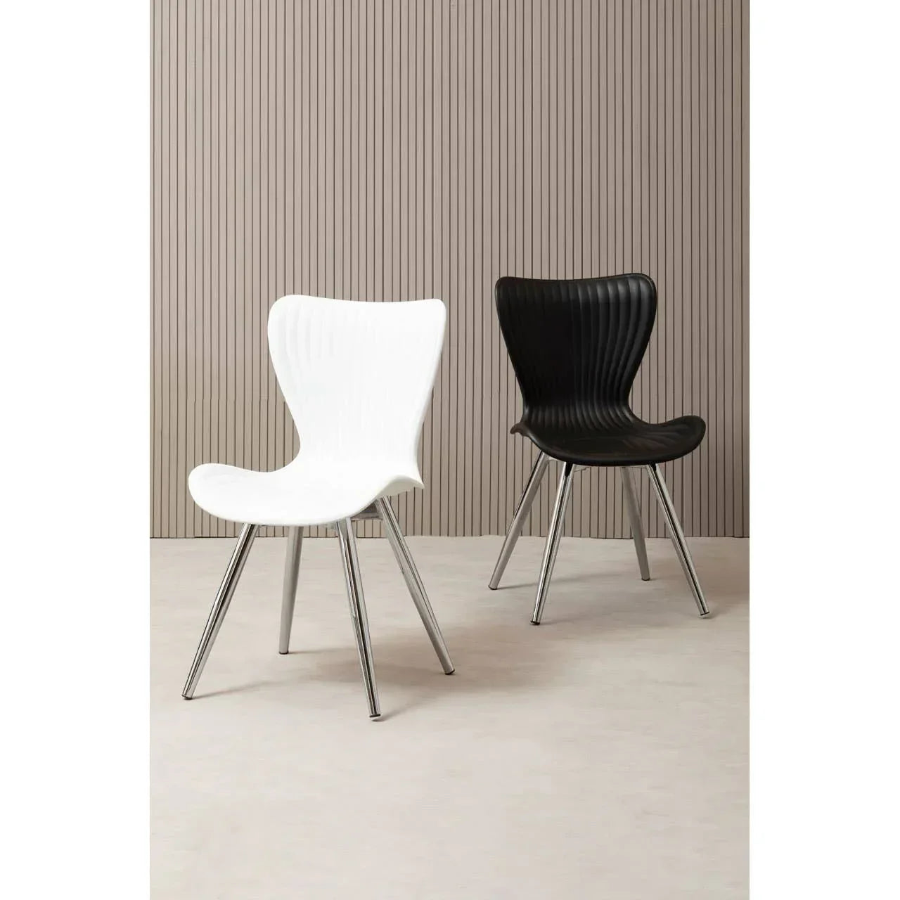 Modern dining chairs with chrome legs, one white and one black, in front of panelled wall
