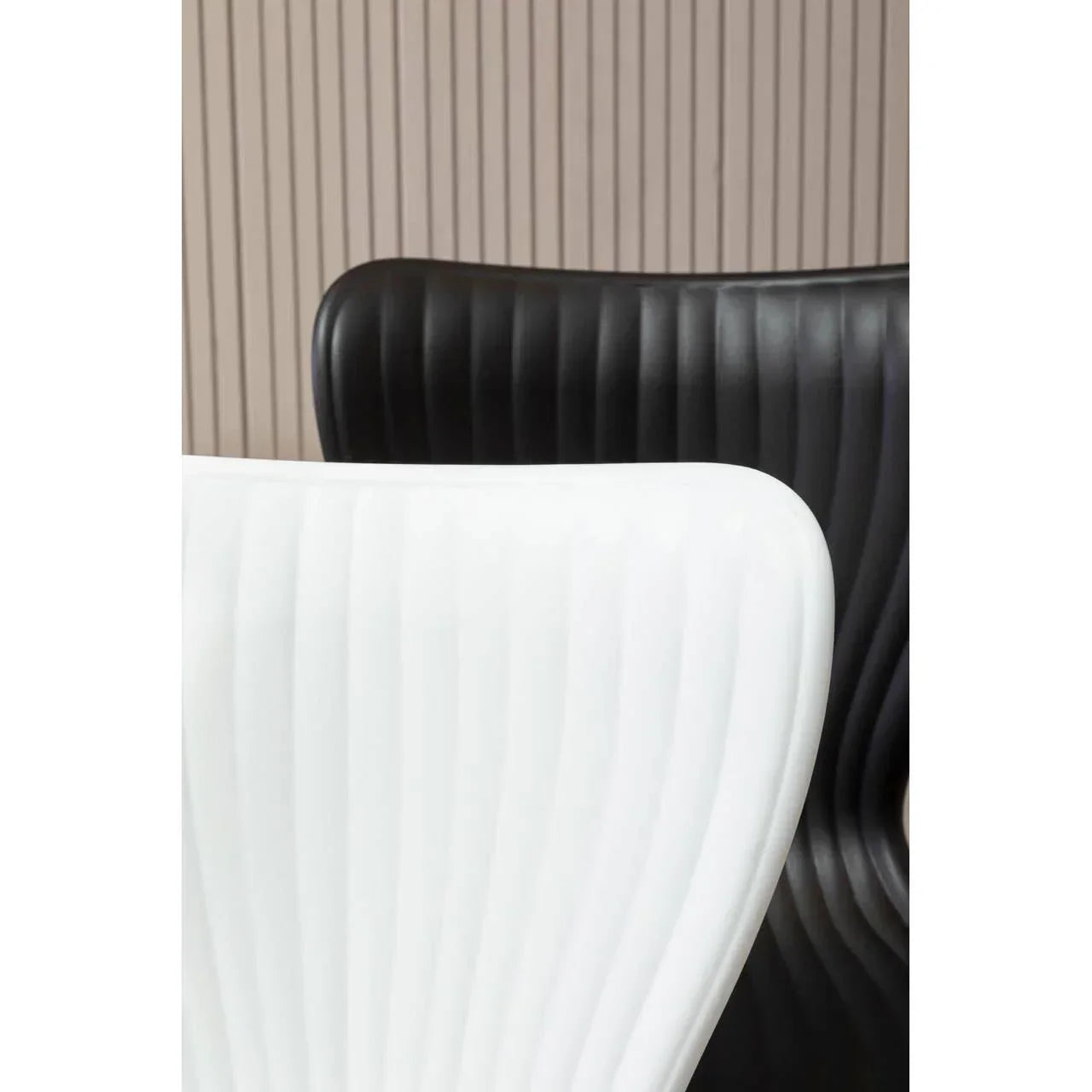 Modern dining chairs in black and white with ribbed backs against a wood panel wall